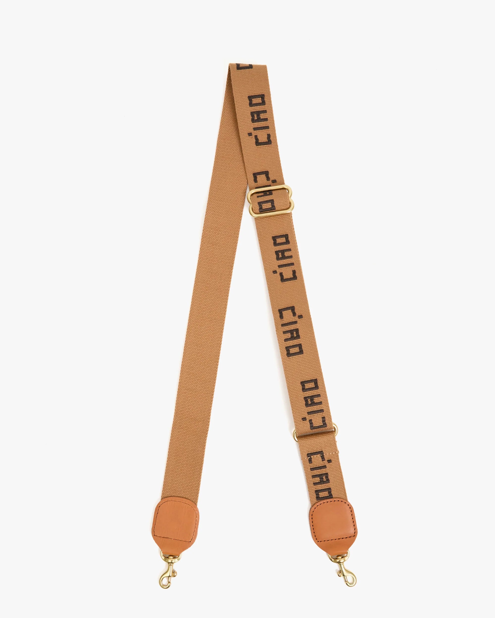 The Clare Vivier Adjustable Crossbody Strap is a tan cotton webbing strap with gold clasps at each end and bold, repeated "ciao" text in black.