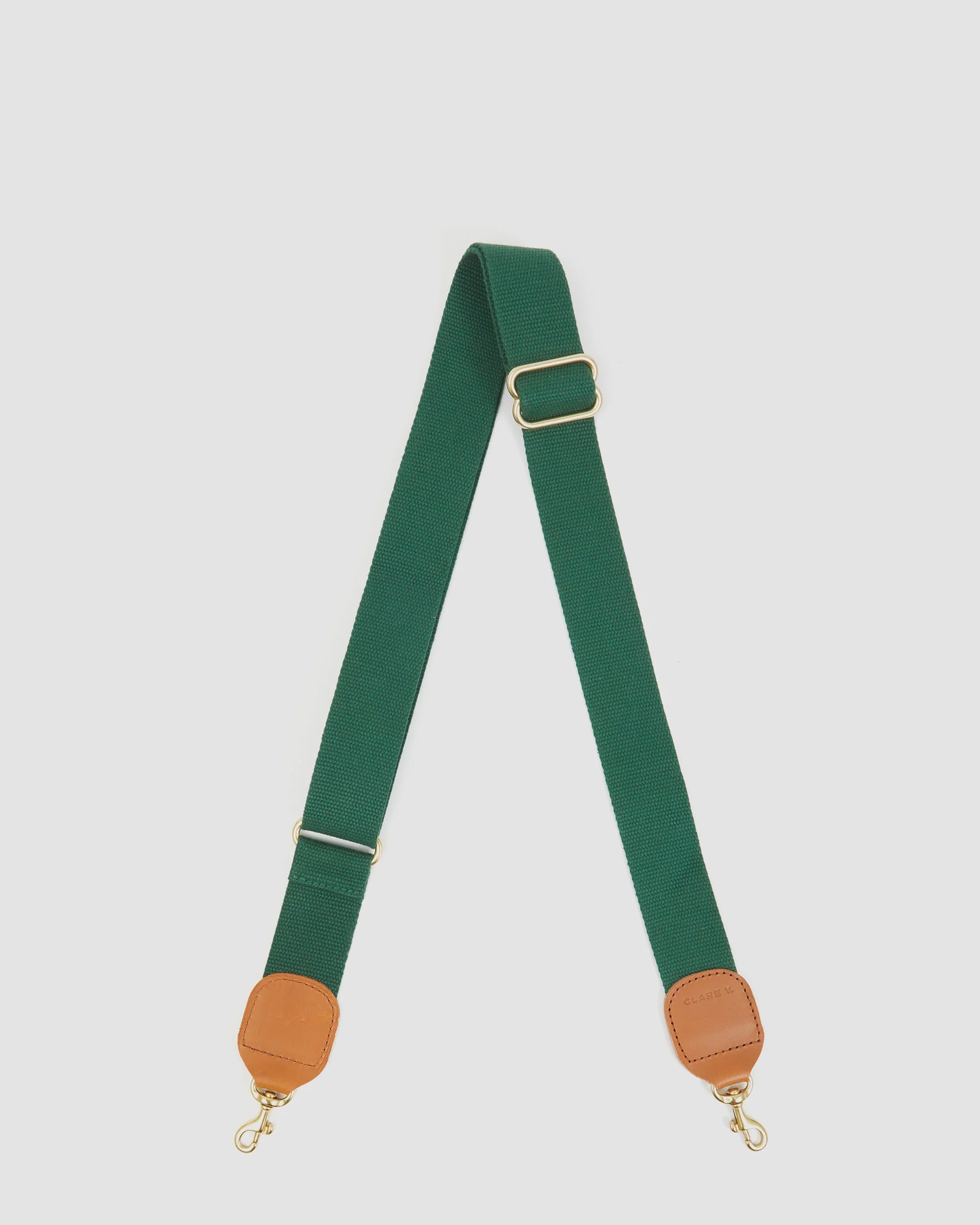 The Clare Vivier Adjustable Crossbody Strap features green cotton webbing, tan leather trim on the ends, and gold metal clips, shown laid flat on a white background.