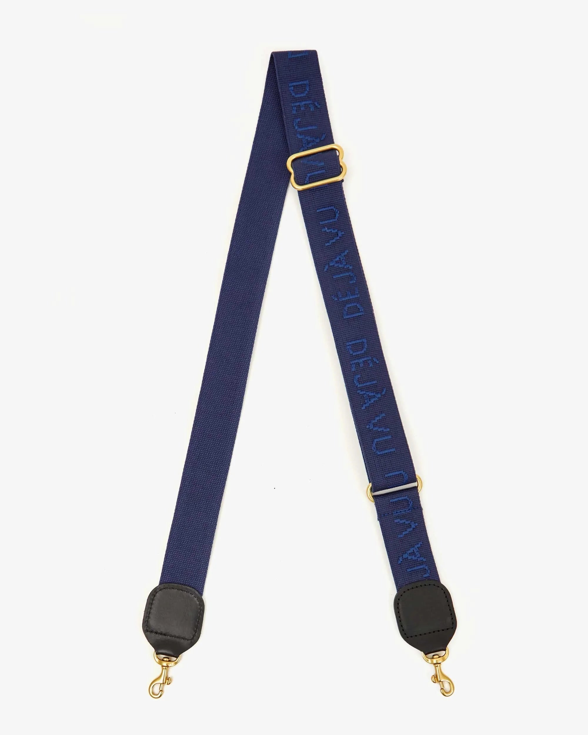 The Clare Vivier Adjustable Crossbody Strap features blue cotton webbing, gold-tone clasps, black leather trim, and raised “DÉJÀ VU” lettering in blue.