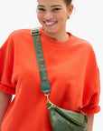 Clare Vivier adjustable crossbody strap on a green SOUVENIR bag, styled with an orange top for a casual look.