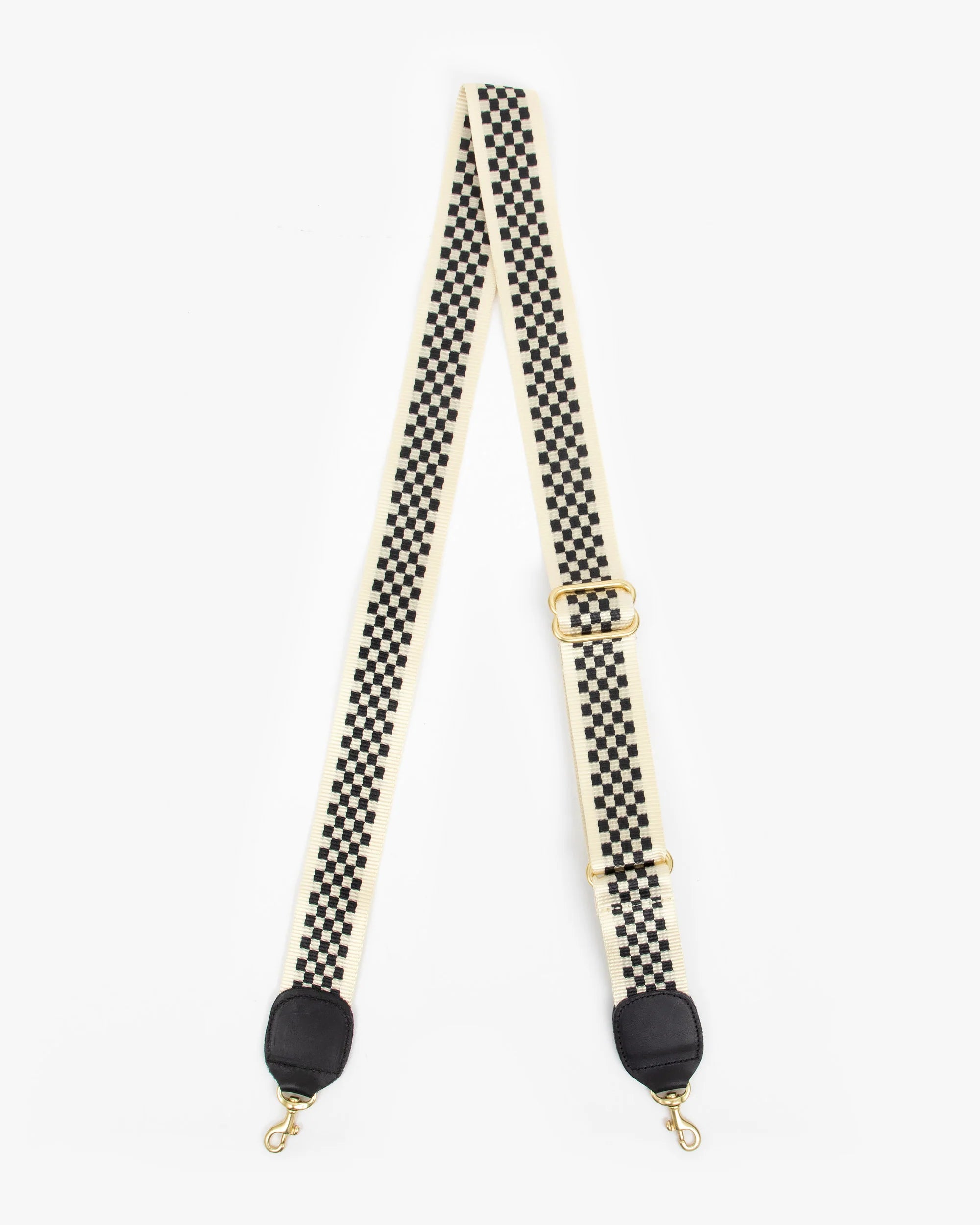 The Clare Vivier Crossbody Strap S25 is a black and white checkered cotton webbing strap with gold clips and black leather ends, adjustable for a crossbody or shoulder bag, shown on a white background.