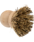 The Be Home Saucepan Brush is a round wooden kitchen brush with stiff, natural vegetable fiber bristles, inspired by timeless design and photographed against a plain white background.