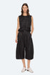 A woman with shoulder-length brown hair and a neutral expression wears the Sea New York Angelina Suiting Culotte, a true-to-size wide-leg black polyester short, styled with a sleeveless peplum top, black belt, and white shoes against a plain background.