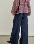 A person models the Connor Wide Leg Pant by Aquarius Cocktail indoors, wearing a red and white checkered long-sleeve shirt. Their hands are in their pockets, the background is plain, and the photo is cropped above the shoulders.