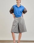 A person stands with hands in pockets, wearing a blue polo shirt, Aquarius Cocktail Coupe Knee Length Short, and black sandals. The background is plain and neutral.