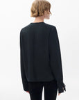 A person with short, wavy, light brown hair is shown from behind wearing the Rag & Bone arden pleated blouse— a black, long-sleeve top with cuff details— paired with black pants against a plain white background.