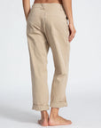 A person stands barefoot with their back to the camera, showcasing ASKK's light beige, rolled-up chino twill pants. These relaxed-fit pants feature visible back pockets and taper slightly at the ankles against a plain white background.