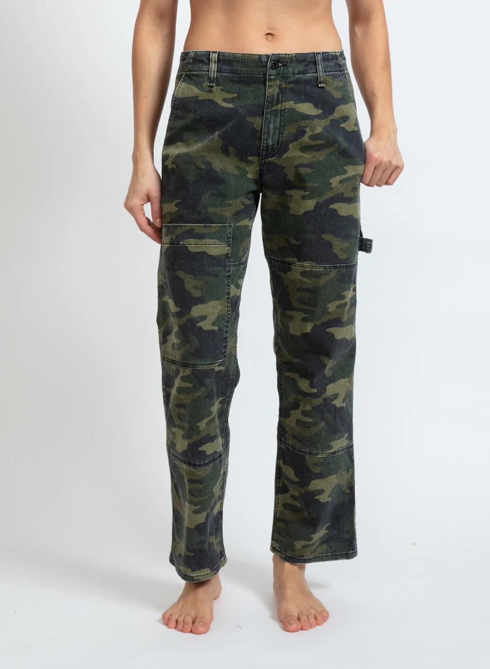 A person stands barefoot against a plain background, wearing the relaxed-fit Carpenter pants from ASKK. These camo cargo pants, crafted from stretch twill, feature practical side pockets and offer a comfortable fit. They are proudly made in Los Angeles. The person's upper body is not visible.