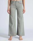 Barefoot against a plain background, a person dons ASKK's Slim Wide Leg jeans. Tailored in Los Angeles with Japanese denim, these light gray, high-waisted jeans feature front pockets and a button closure.