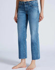 A person stands barefoot in ASKK's Low Rise Straight Studded jeans, crafted from Japanese denim. The jeans feature a straight-leg cut with frayed hems, creating a striking contrast against the plain, light-colored background.