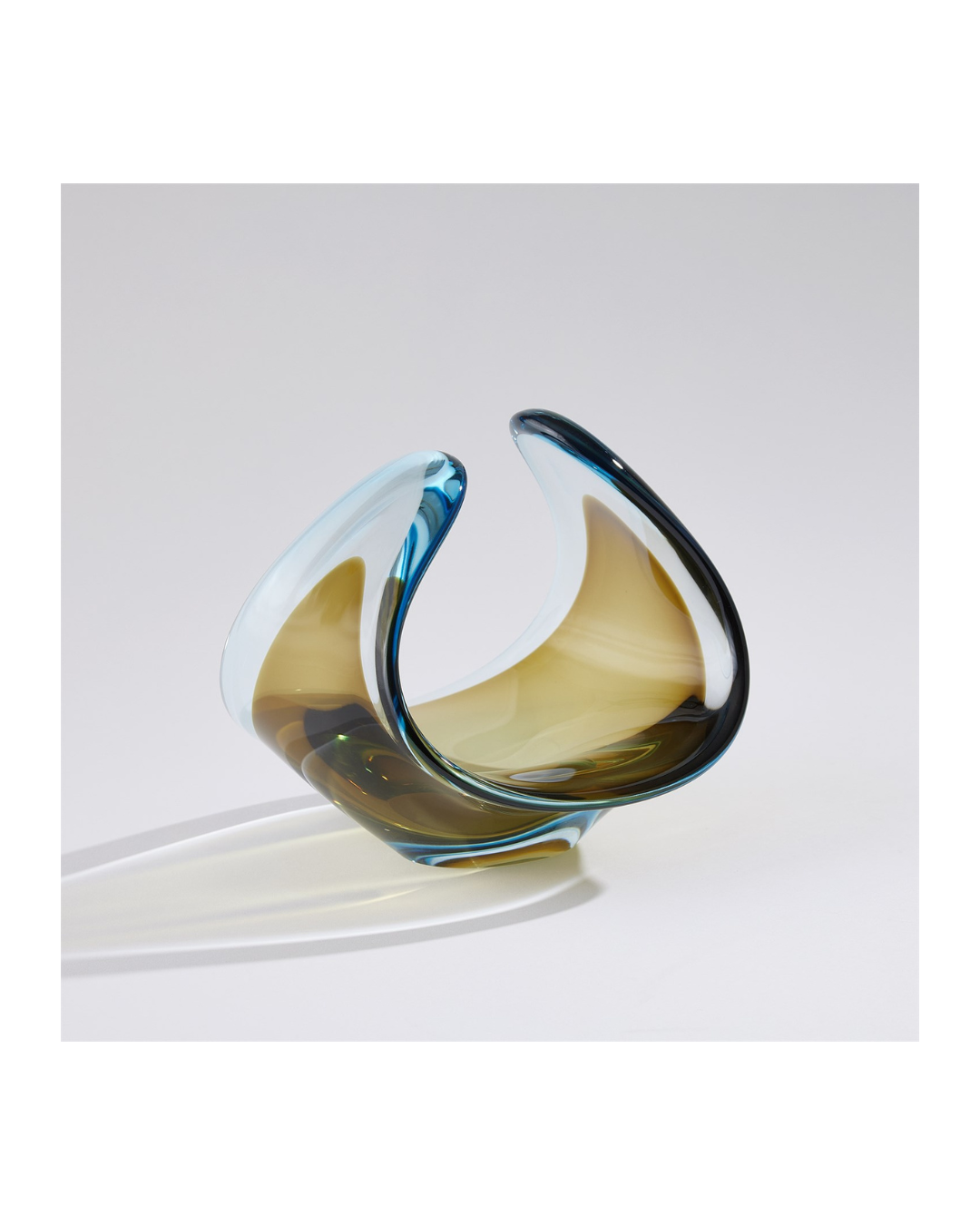 The Duet Bowl-Turquoise/Beige by Global Views features captivating Polish art glass with smooth curves and seamless turquoise and beige hues. Its reflective surface and unique shape provide an elegant, dynamic look against a plain white backdrop.