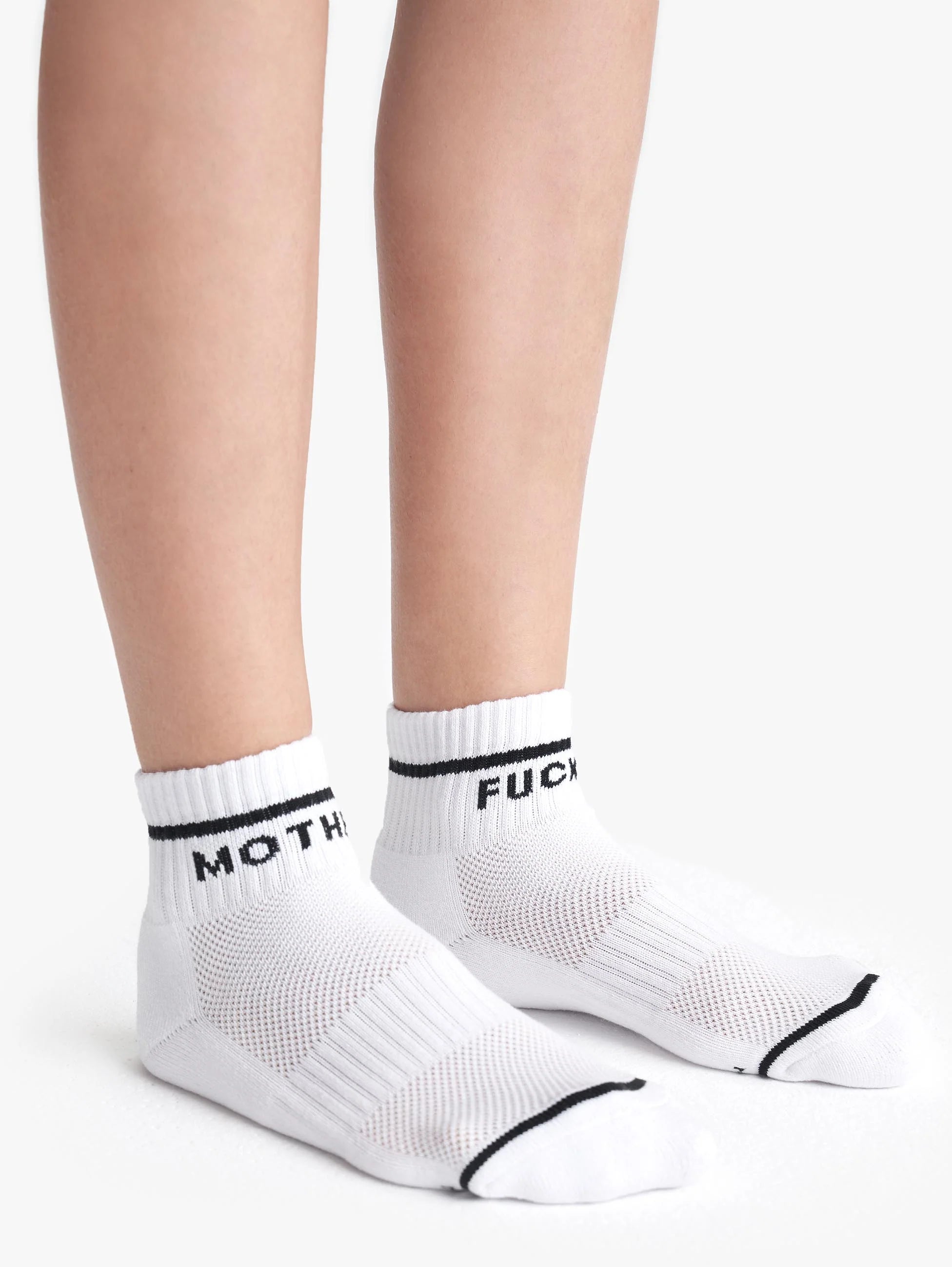 A person wears Mother’s Baby Steps Ankle socks—classic black and white tube socks with bold black stripes and the words “MOTH” and “FUCK” printed in black around the cuffs.