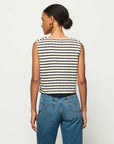 A person with short hair tied back is standing against a white background, wearing the Bettina Tank from Nation LTD, a boxy sleeveless top in black-and-white stripes made of soft Peruvian cotton, paired with blue jeans.