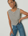 A person wears the Nation LTD Bettina Tank, a striped, sleeveless top made from soft Peruvian cotton with gold shoulder buttons, paired with blue jeans. Hoop earrings complete the look against a plain backdrop.