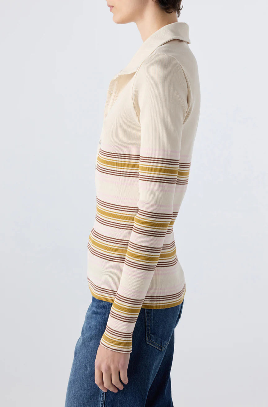 A person wearing the AMO Denim Desiree Tee, a cream-colored ribbed top with yellow, brown, and pink stripes, paired with blue jeans, stands sideways against a plain light background.