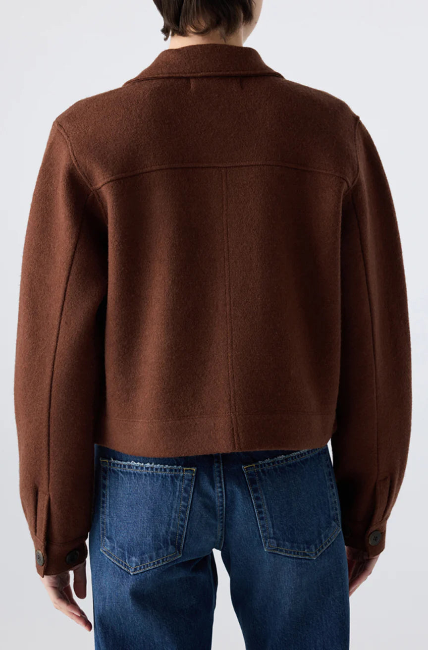 Model shown from the back in the AMO Denim Isabelle Jacket, a brown, collared, long-sleeve cropped trucker with large cuffs, paired with blue jeans against a plain light background for a flattering silhouette.