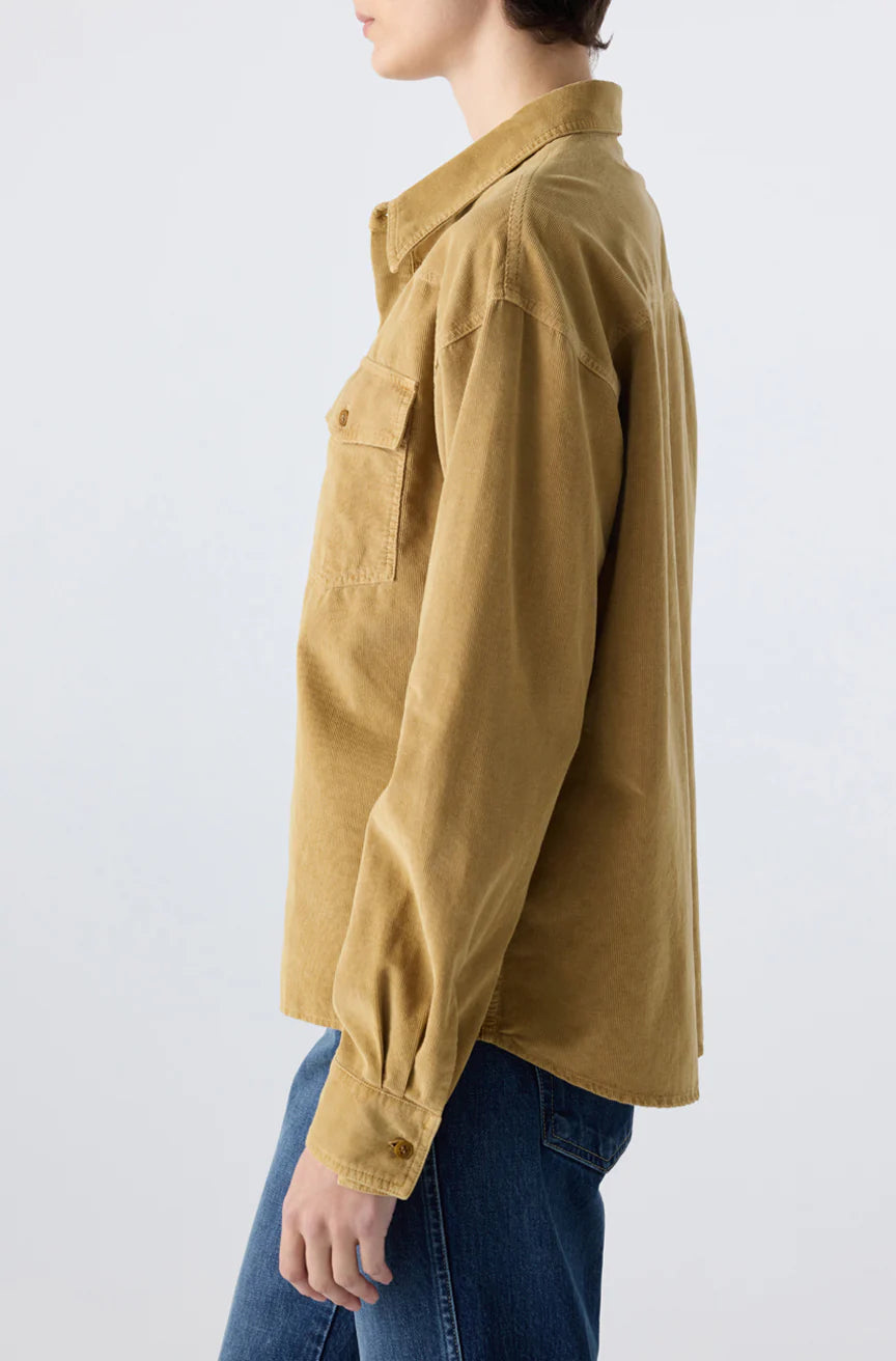 A person wearing the AMO Denim Jenn Shirt, a loose-fitting tan corduroy top with a western-style chest pocket, paired with blue jeans and shown from the side against a plain light background.