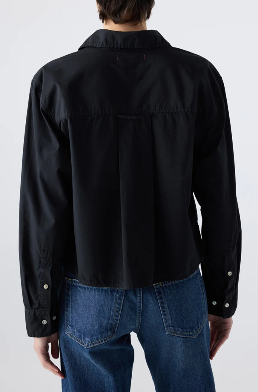 A person is seen from the back against a plain light background, wearing the AMO Denim Ruth Crop Shirt in black with long sleeves and blue jeans.