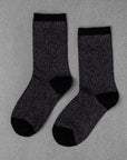 A pair of Unified Glitter Socks featuring a black base with multicolored speckles, plus black toes, heels, and cuffs, is laid flat on a gray surface.