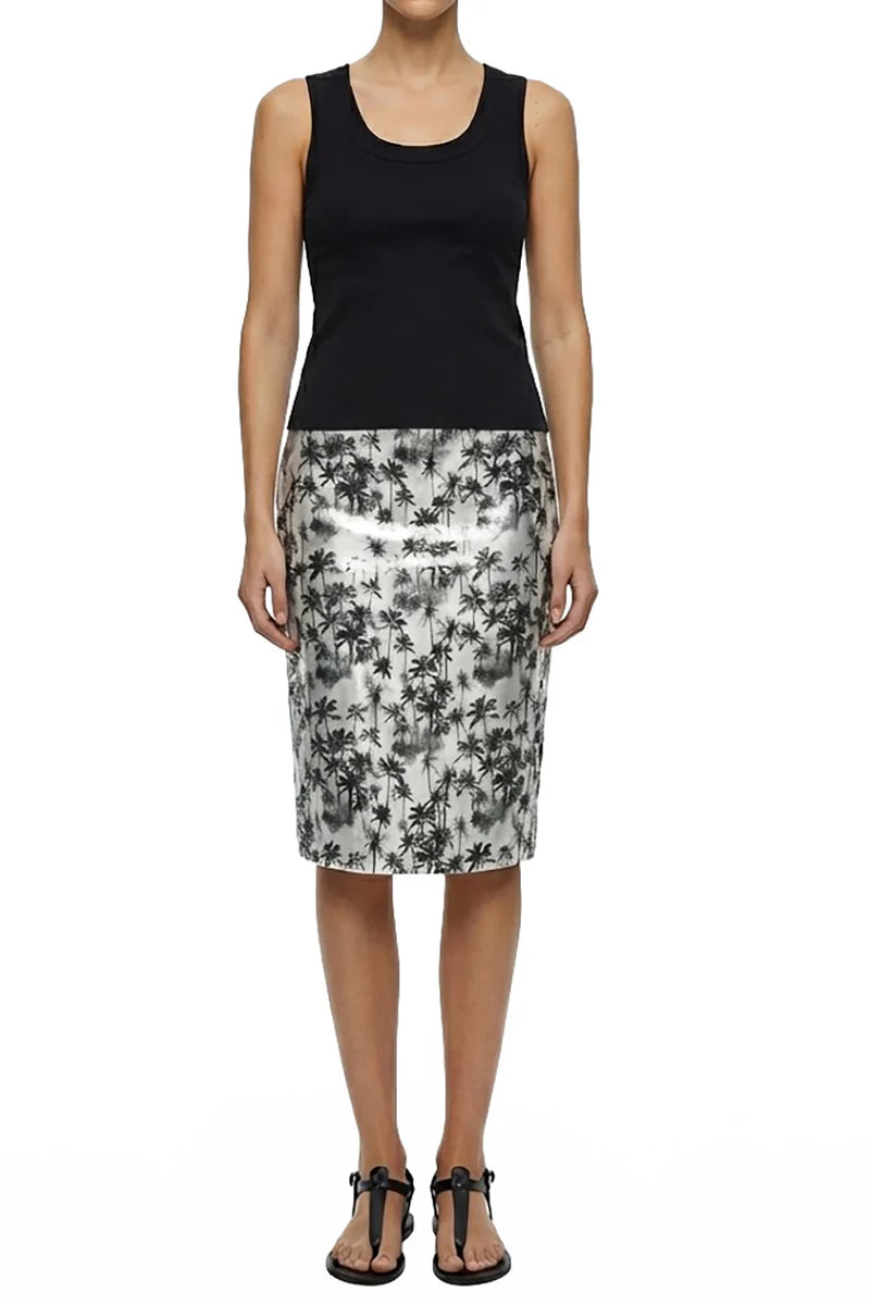 A woman stands facing forward in a sleeveless black tank top, Le Superbe's Black Palms Pencil Skirt with a bold palm print, and black sandals.