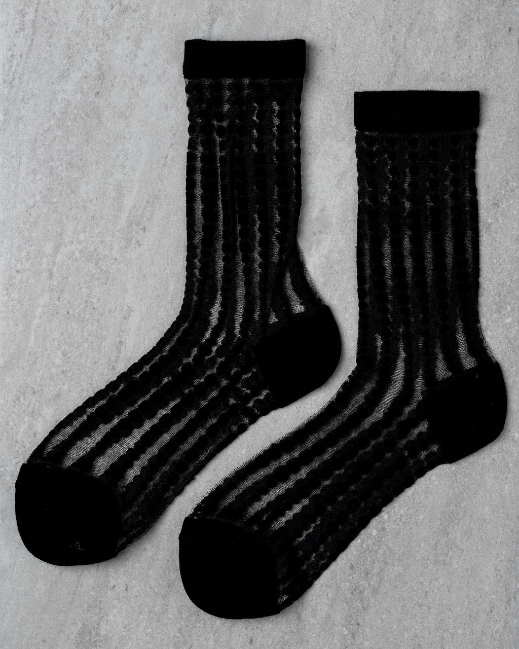 The Unified Sheer Bubble Sock features a black sheer crew design with wavy vertical stripes, shown side by side on a light gray background—ideal for elevating your everyday look.