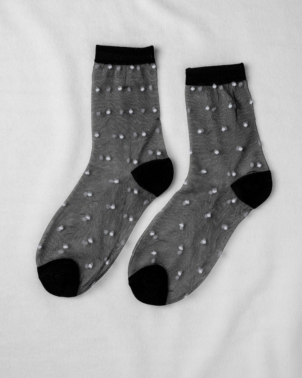 Sheer Dot Socks by Unified: sheer black socks with small white dots and solid black toes, heels, and cuffs—stylish women’s accessories displayed flat on a white surface.