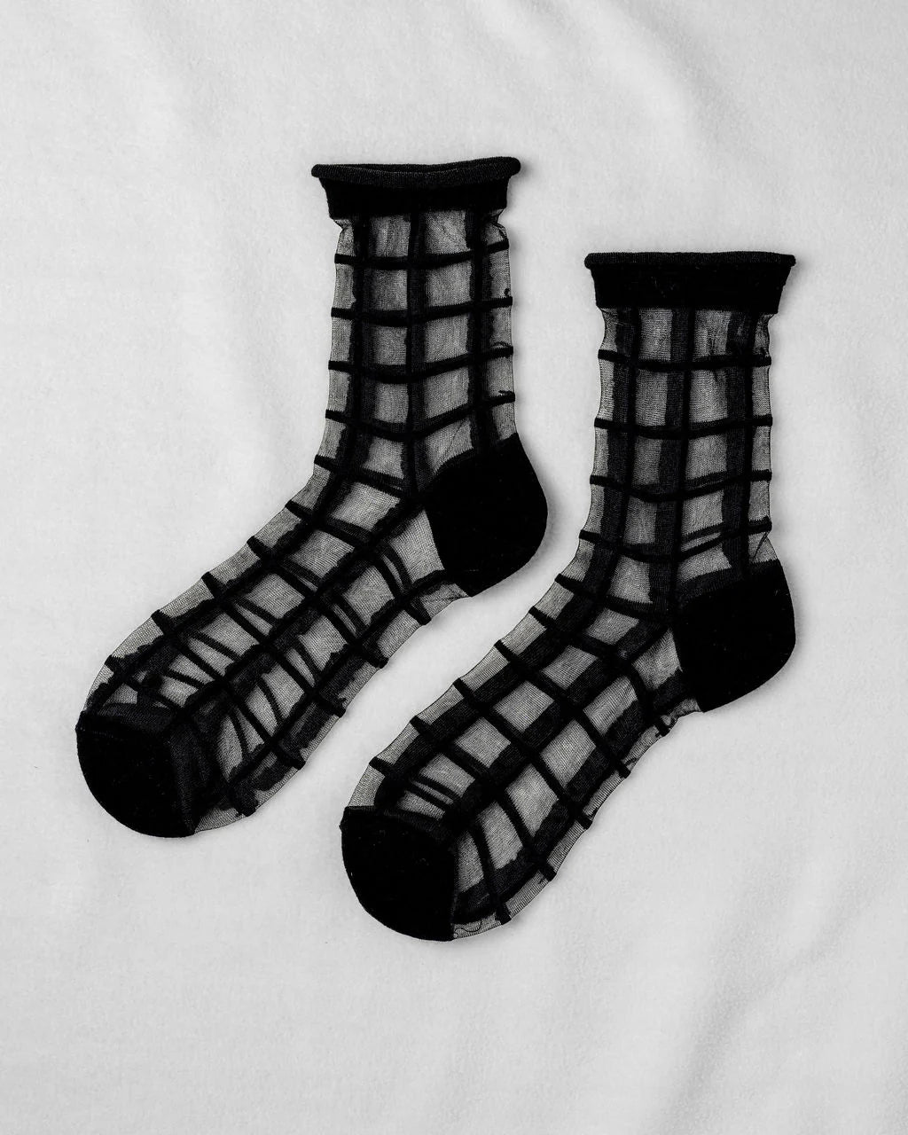 The Unified Sheer French Window socks feature a bold grid pattern with solid black cuffs, heels, and toes, displayed flat on a white background.