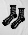 The Unified Sheer French Window socks feature a bold grid pattern with solid black cuffs, heels, and toes, displayed flat on a white background.