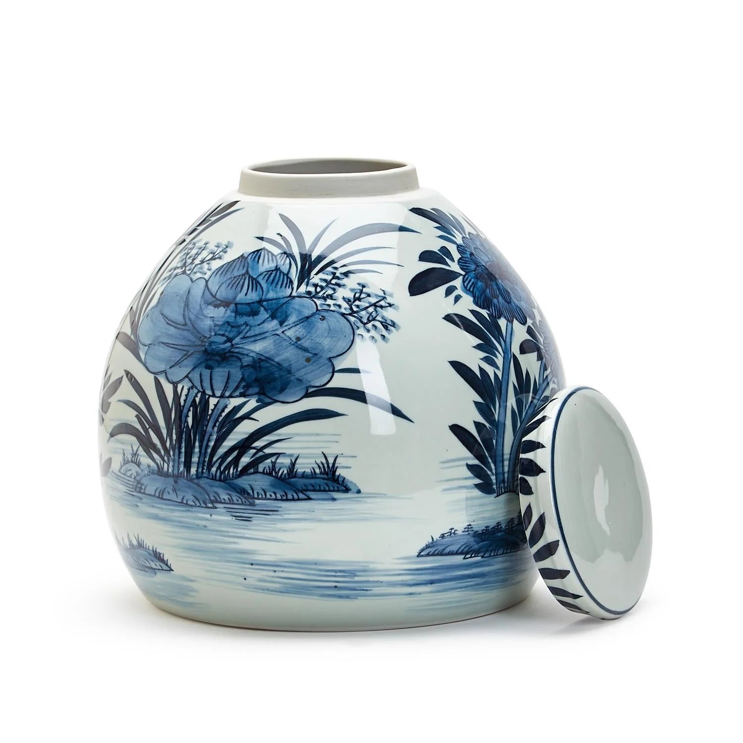The Blue White Ginger Jar by Two's Company is a round porcelain jar featuring blue floral and water scene designs, shown on a white background with its matching lid placed beside it.