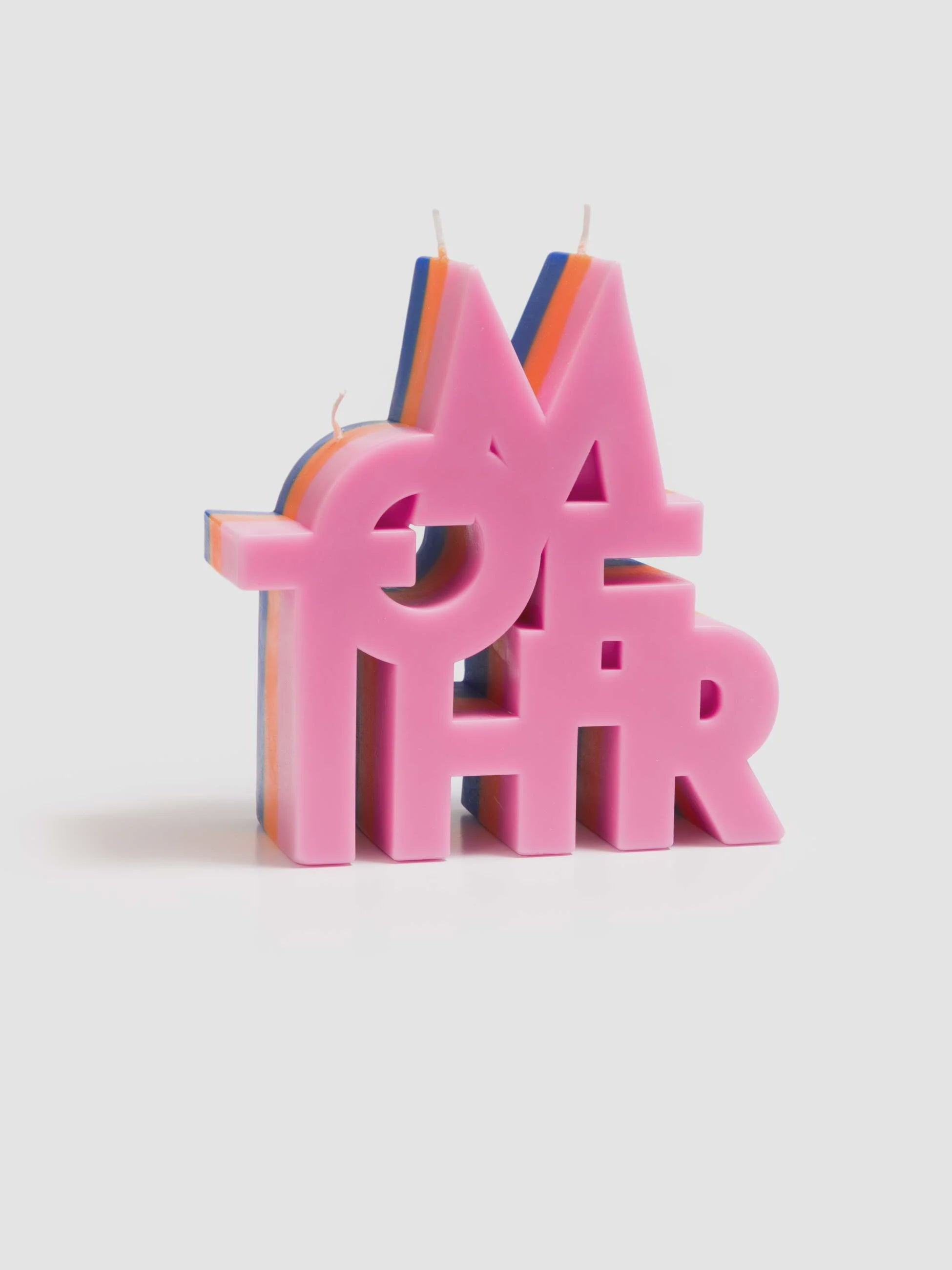 The Mother Burnout Candle by Mother features stacked, overlapping "MOTHER" letters in pink with visible blue, orange, and white soy wax layers. This colorful three-wick candle is displayed against a plain light background.