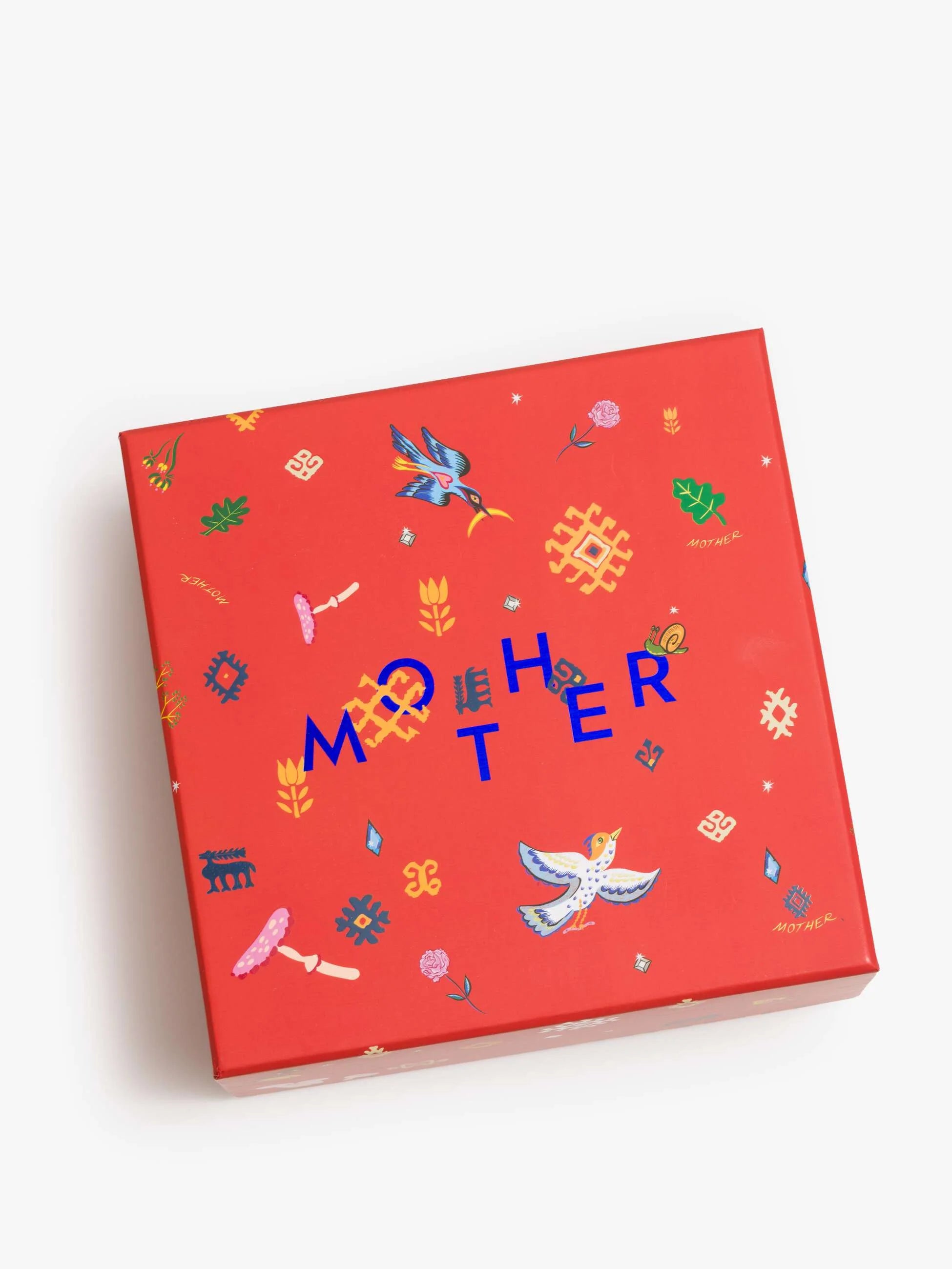 The Mother Burnout Candle by Mother features a vibrant box in blue, orange, and pink with bold "MOTHER" text. Inside is a luxurious three-wick soy wax candle.
