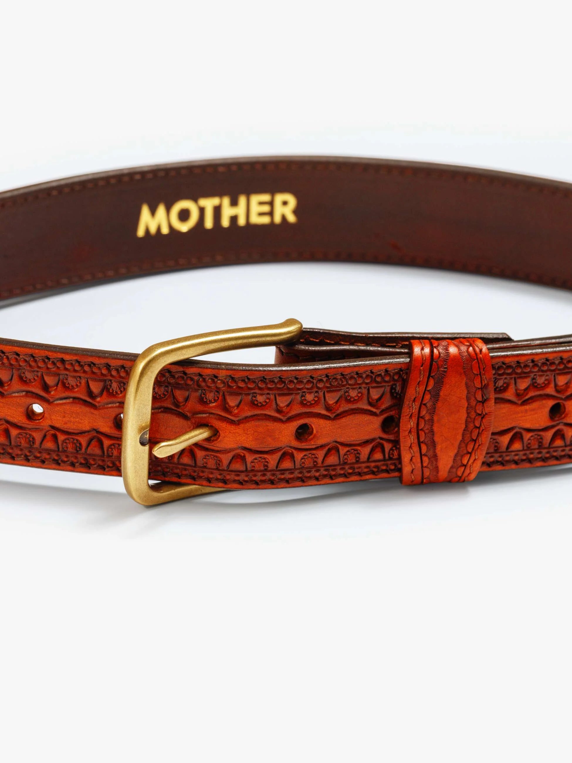 The Eye Opener by Mother is a vintage cow leather belt with decorative patterns and a gold buckle, featuring "MOTHER" printed in gold on the inner side.