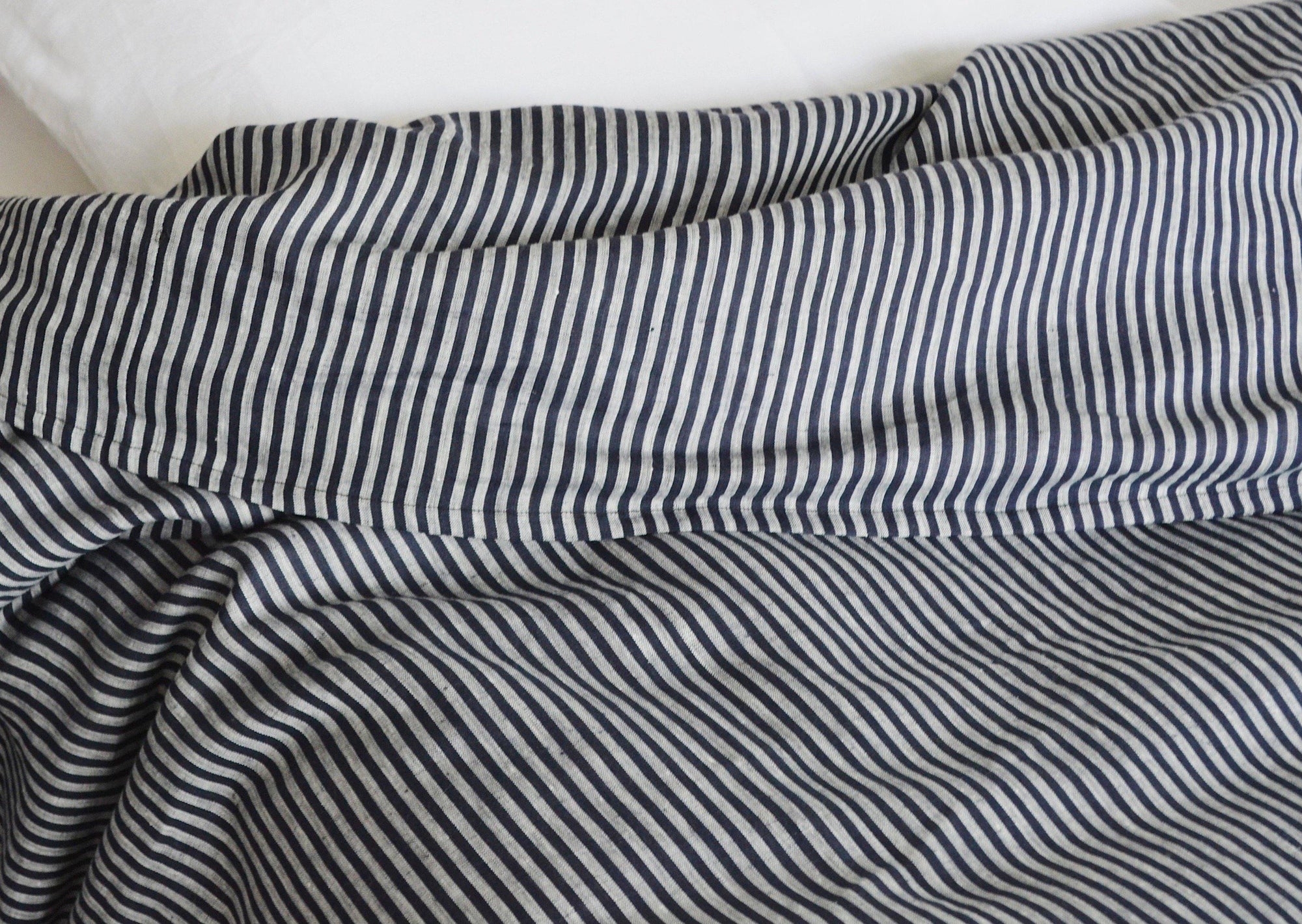 A close-up of a rumpled bed featuring the Modernplum Baltic King Duvet, showcasing black and white vertical stripes, with a white pillow in the background.
