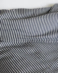 A close-up of a rumpled bed featuring the Modernplum Baltic King Duvet, showcasing black and white vertical stripes, with a white pillow in the background.