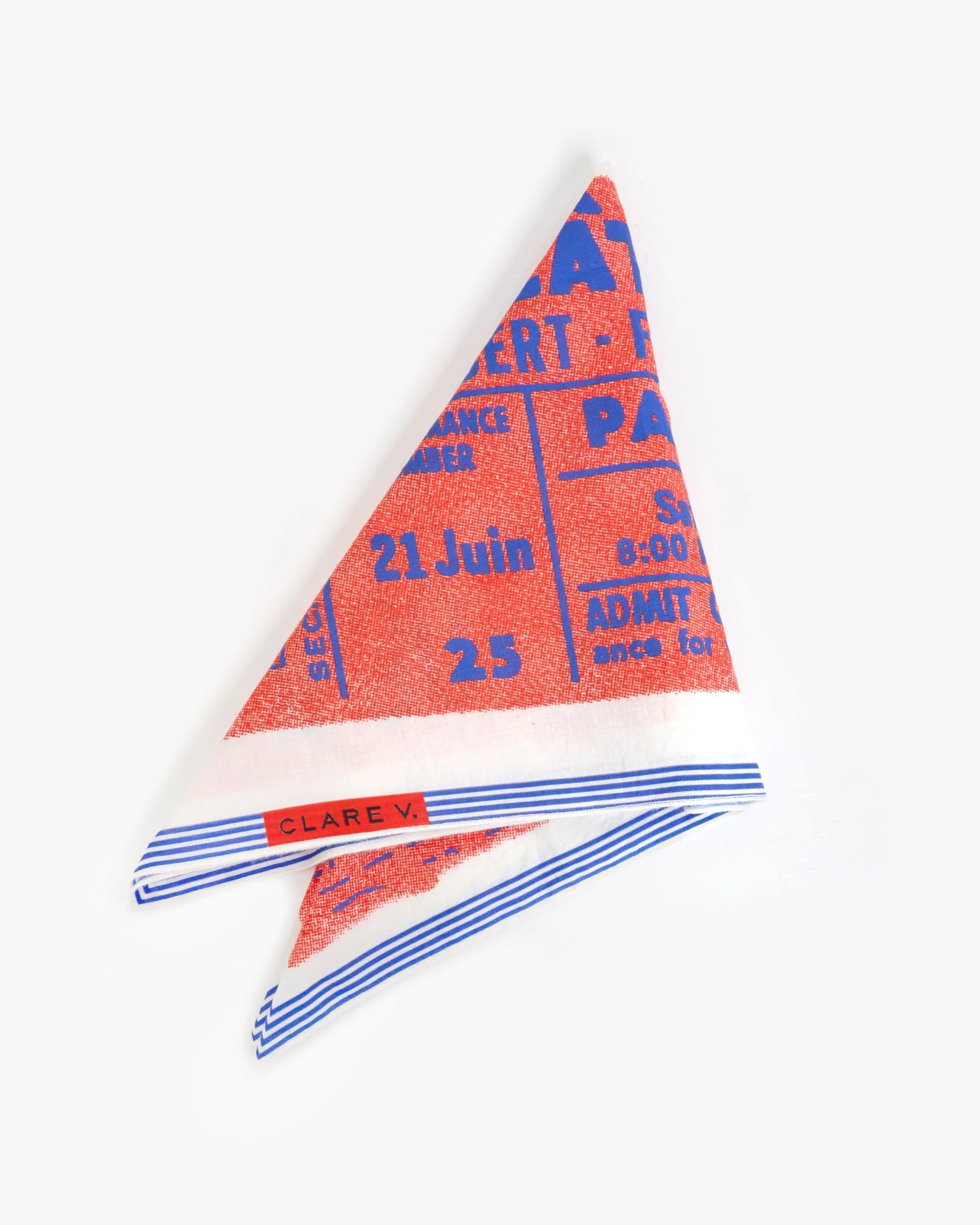 The Clare V Bandana by Clare Vivier is a 20 x 20-inch cotton scarf in red, blue, and white with French text like a concert ticket, striped edges, and a "CLARE V." label sewn in one corner. Photographed on a plain white background.