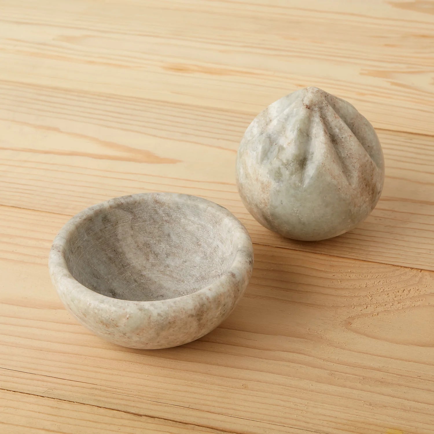 The Be Home Waterfall Marble Citrus Press, featuring a gray and white marble design with a ridged reamer and matching handmade bowl, sits on a light wood surface.