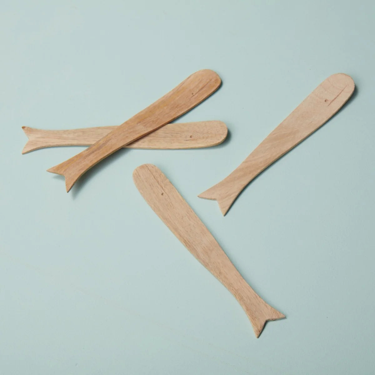 The Be Home Sydney Whale Spreaders S/4 are handcrafted from sustainably sourced mango wood and feature whale-inspired shapes. Arranged on a light blue surface, these unique utensils add charm to any table setting.
