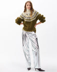 A woman stands against a white background wearing the Rag & Bone beth oversized fair isle tneck, styled with shiny metallic silver wide-leg pants and pointed dark ankle boots. Her hands are on her hips and her hair is loose.