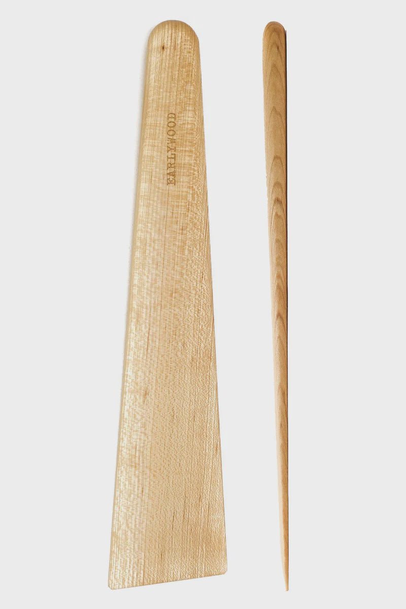 Two wooden kitchen utensils are displayed on a white background. The top item is a flat, rectangular spatula with rounded edges, branded as "EARLYWOOD," ideal as the best spatula for cast iron pans. Below it is the EWood Big Tera Scraper by Faire, a slim, tapered hardwood utensil resembling a dowel or mixing stick, perfect for all your kitchen needs.