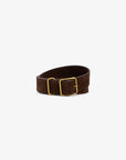 The Janessa Leone Bowe Belt, made from dark brown Italian suede with a rectangular gold custom hardware buckle, is shown coiled in a loose roll on a plain white background.