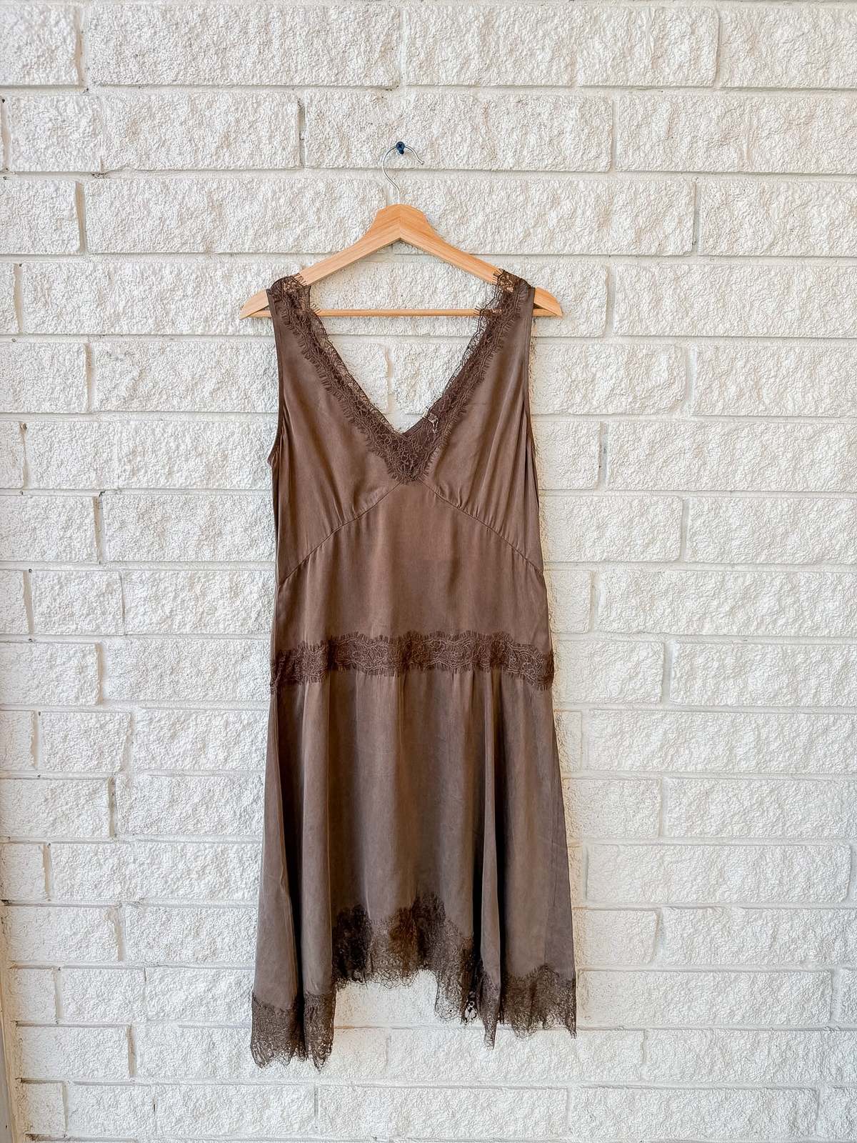 Lace-trimmed brown cupro viscose slip dress by Xirena on hanger against white brick wall at Bungalow Furniture &amp; Accessories.