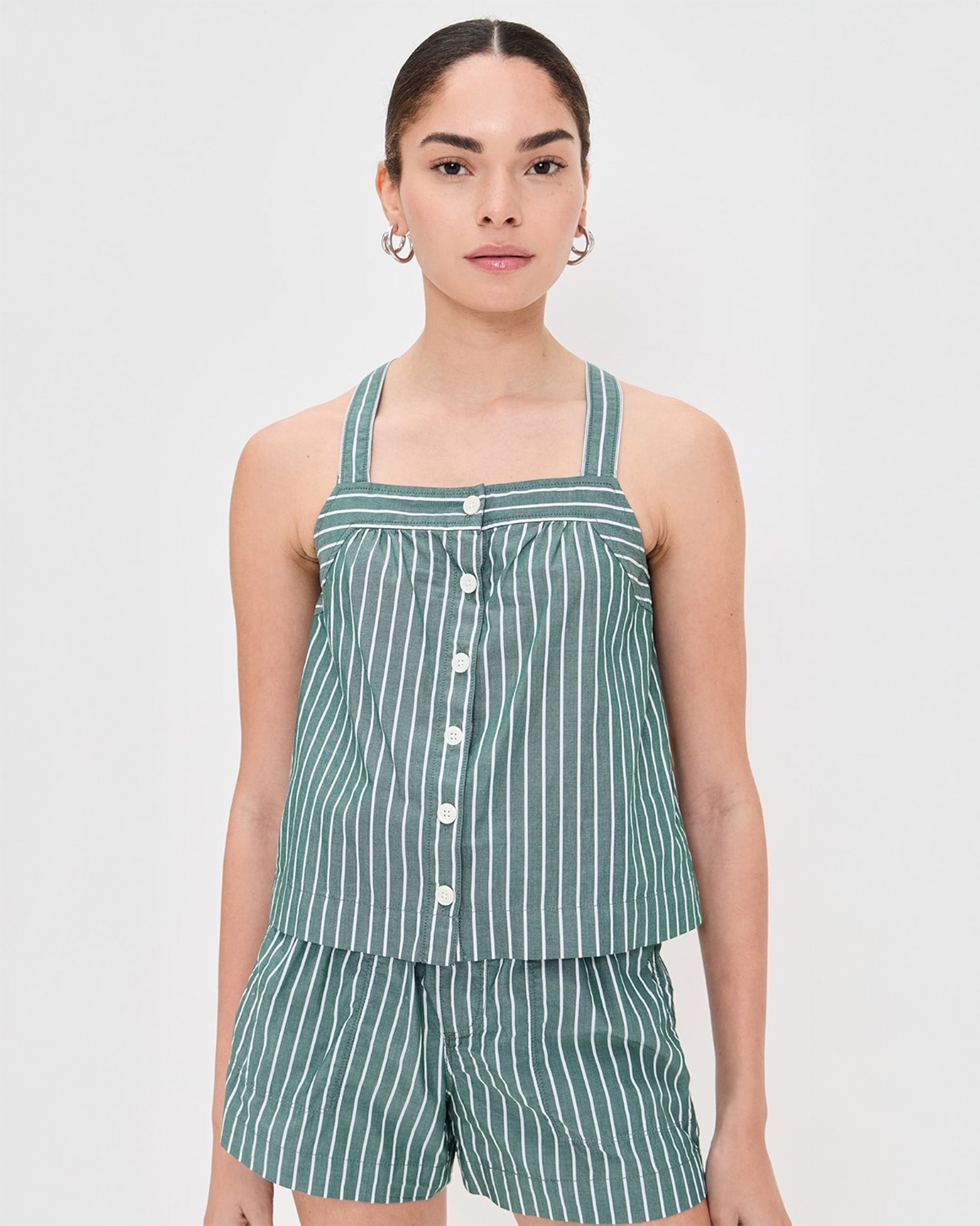A person wears the Leah Top In Stripes by Alex Mill—a green and white vertically striped sleeveless button-down—paired with matching lightweight shorts, standing against a plain light background.