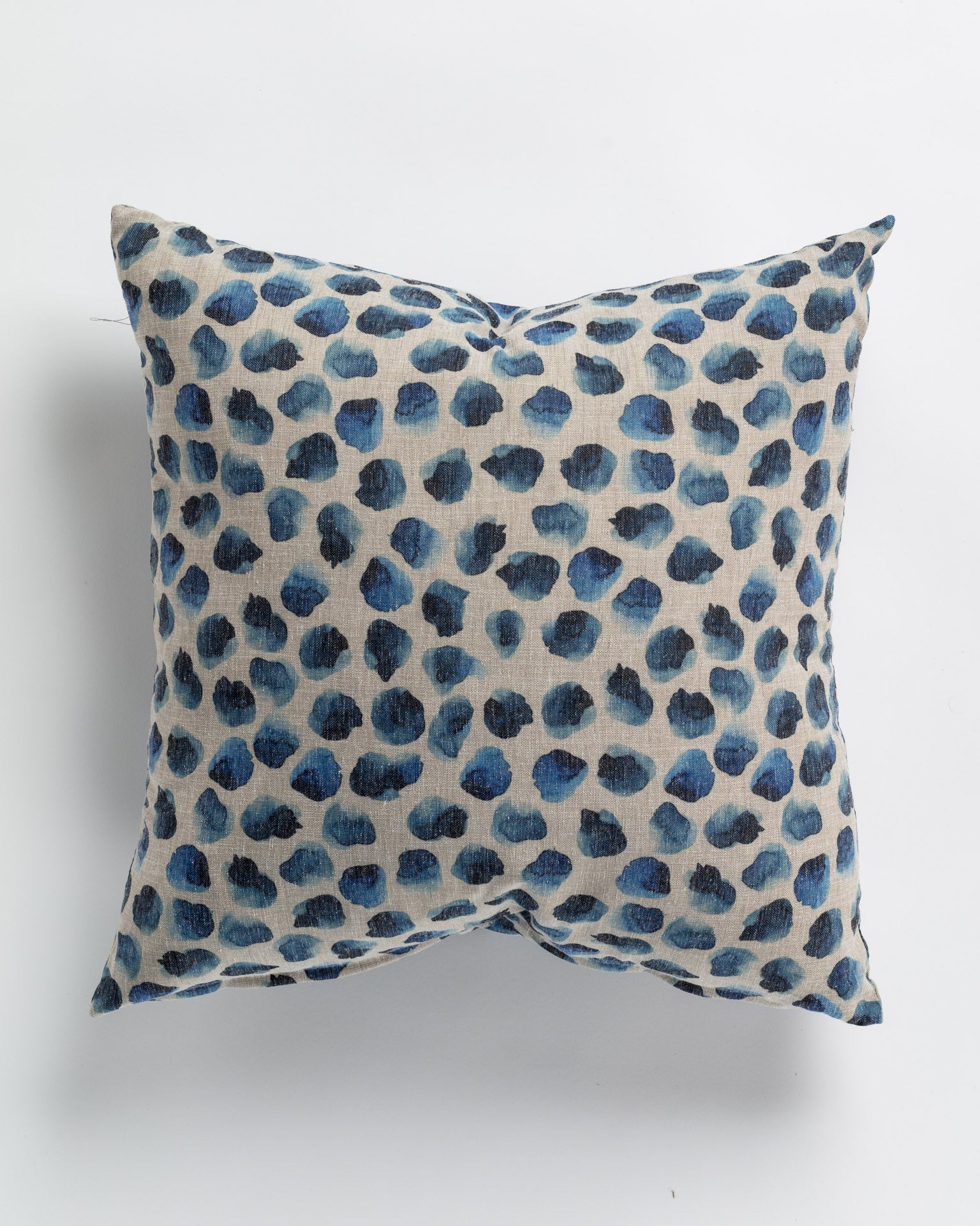 A Blurry Dot Indigo Pillow 26x26 with a pattern of blue leopard spots on a beige background, photographed against a white surface in Scottsdale Arizona by Gabby.