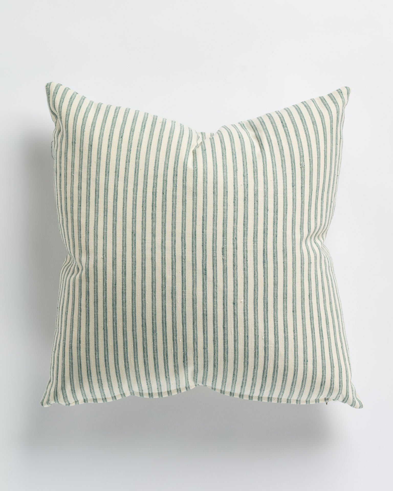 A Bones Blue Spruce Pillow 26x26 by Gabby with pale beige and soft green vertical stripes on a neutral background, photographed frontally against a plain white surface in a Scottsdale Arizona bungalow.