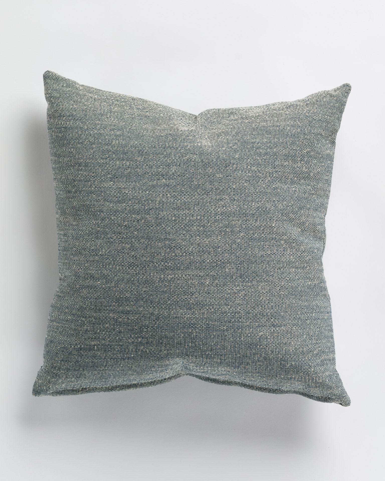 A Cross Stitch Sapphire Pillow - 26x26" by Gabby, with a textured gray fabric, displayed on a white background. The pillow, crafted in the style of a Scottsdale Arizona bungalow, appears soft and neatly sewn with an even fill.