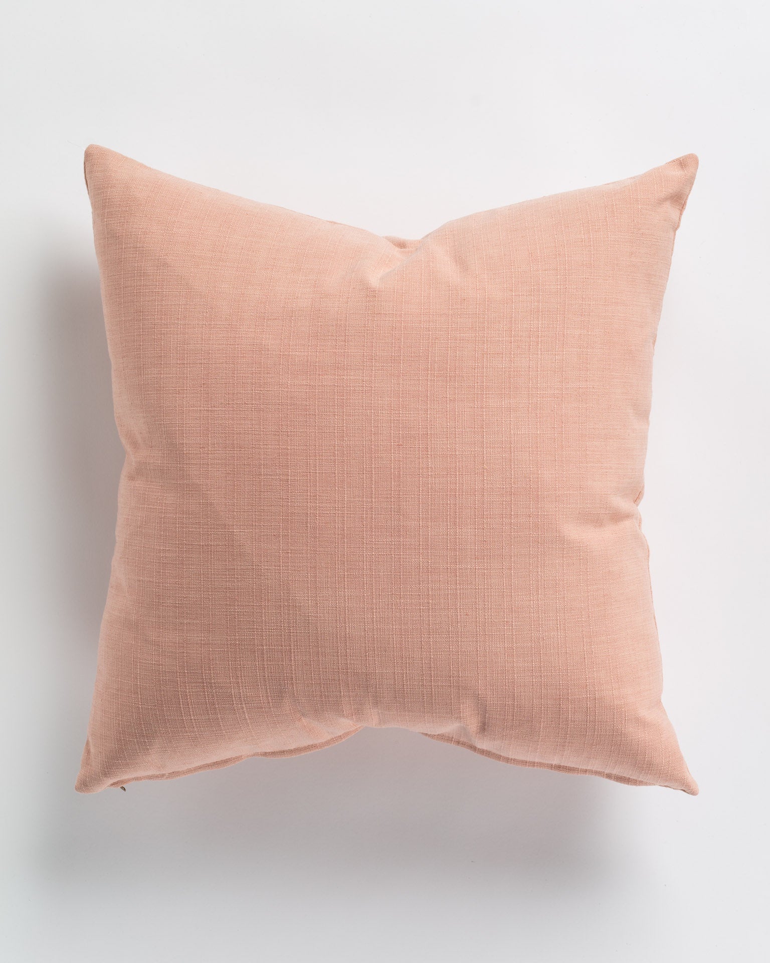 A square cushion with a soft, peach-colored fabric cover. The fabric appears to have a subtle woven texture, and the Gabby Splendor Nude Pillow 26x26 is placed on a plain white background. The corners of the pillow are slightly creased, giving it a relaxed look.