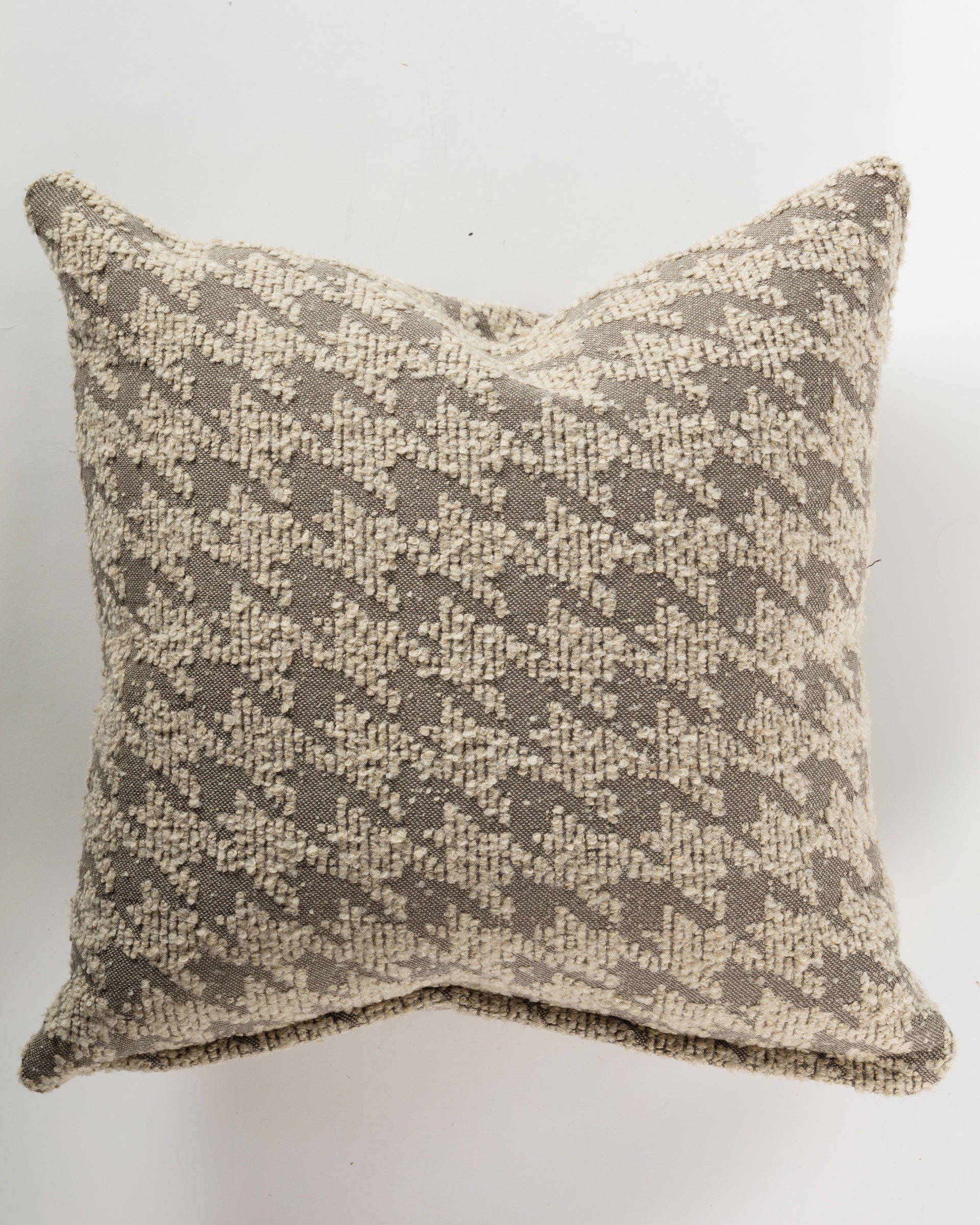 The Gabby Mega Houndstooth Pillow 26x26 is an ultra-luxurious square pillow showcasing a beige and taupe houndstooth pattern. Crafted from textured fabric, it offers a soft touch that enhances home decor. Complete with a pillow insert, it stands out elegantly against a simple, light background.