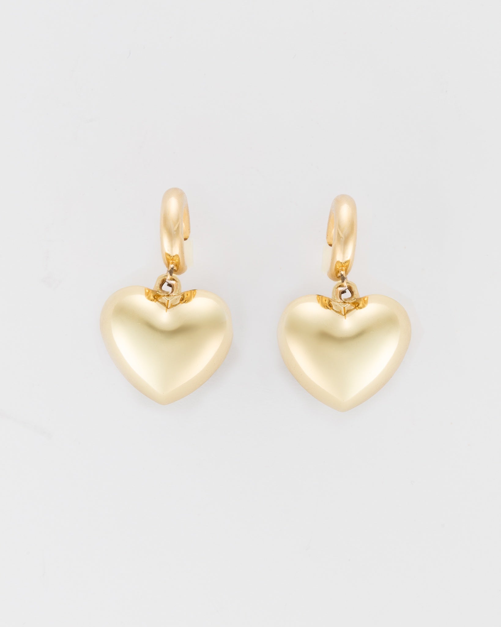 A pair of Bubble Heart Earrings by Lucky Star with a smooth, polished finish. Each heart is attached to elegant gold hoop clasps, creating a simple yet sophisticated design. The jewelry is displayed against a plain white background.