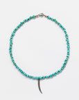 A Designs By Raya necklace featuring a string of turquoise beads, styled in the Arizona fashion, with a central, silver-colored, curved horn pendant against a white background.