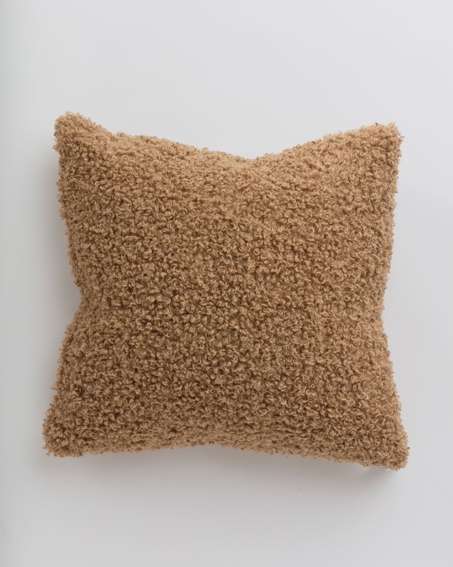 A fluffy, soft, light beige Curly Camel Pillow 26x26 with a textured surface, showcased against a plain white background in a Scottsdale Arizona bungalow by Gabby.